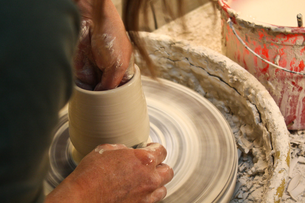 A potter's hands at the wheel in a sunlit studio.